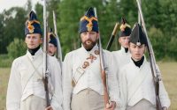 Soldiers marching in historical military uniforms reenact past events outdoors.